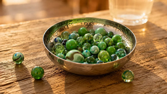 Bol en métal patiné rempli de billes vertes en verre posé sur une table en bois rustique, lumière chaude de fin de journée.